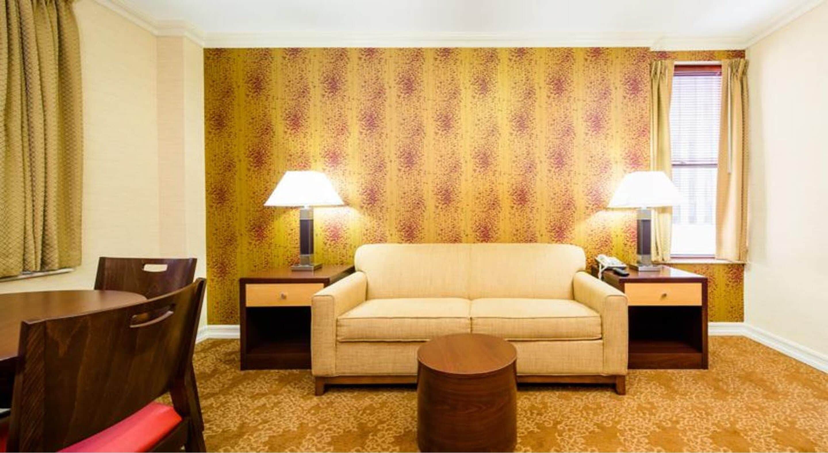Una habitación con sofá, dos mesitas de noche con lámparas, una silla de madera y una pequeña mesa redonda.