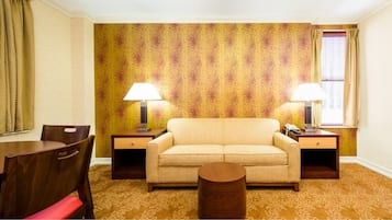 Una habitación con sofá, dos mesitas de noche con lámparas, una silla de madera y una pequeña mesa redonda.