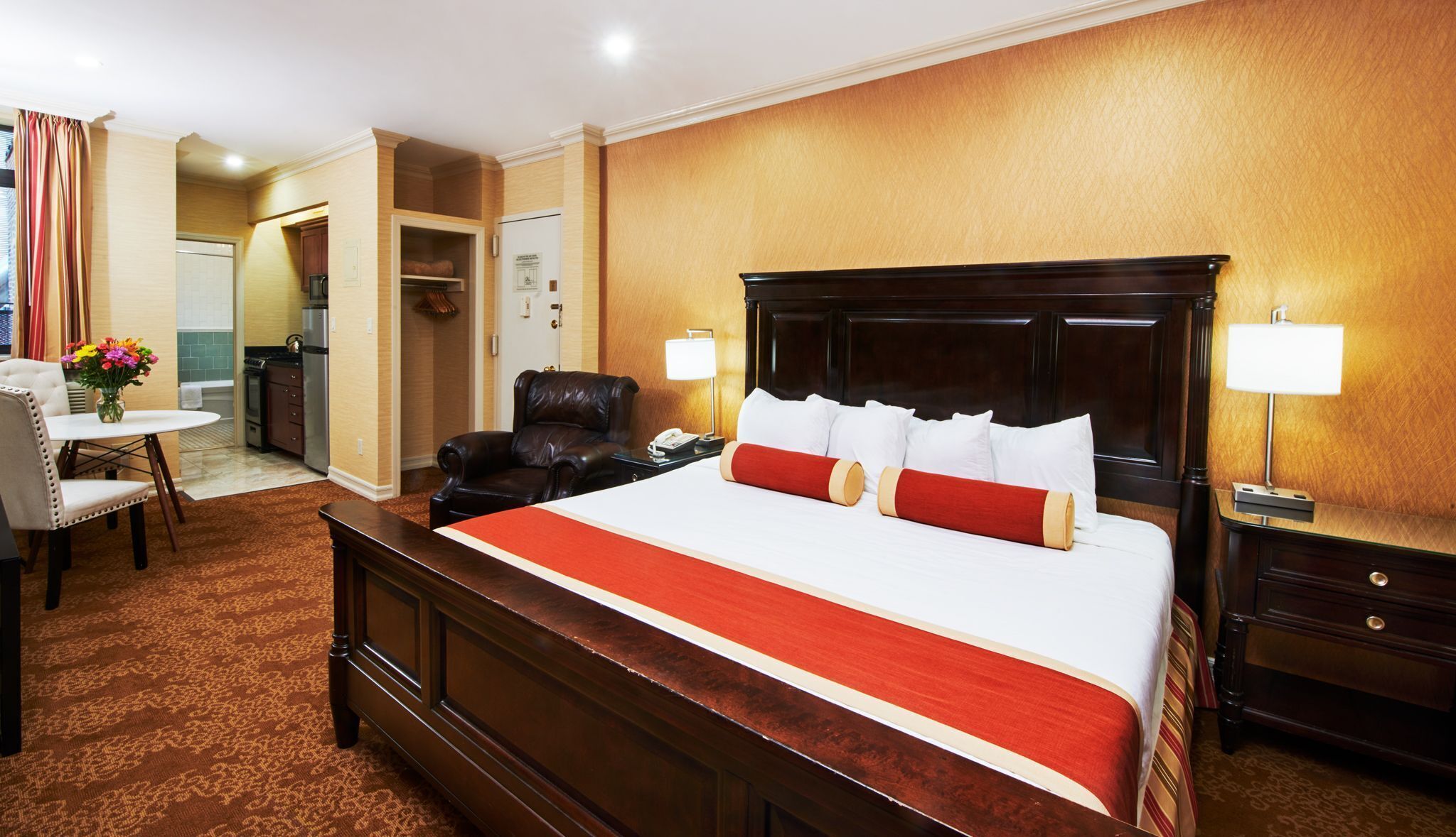 Quarto de hotel com uma cama grande, uma escrivaninha com cadeira, uma mesa de jantar com cadeiras e uma área de cozinha.