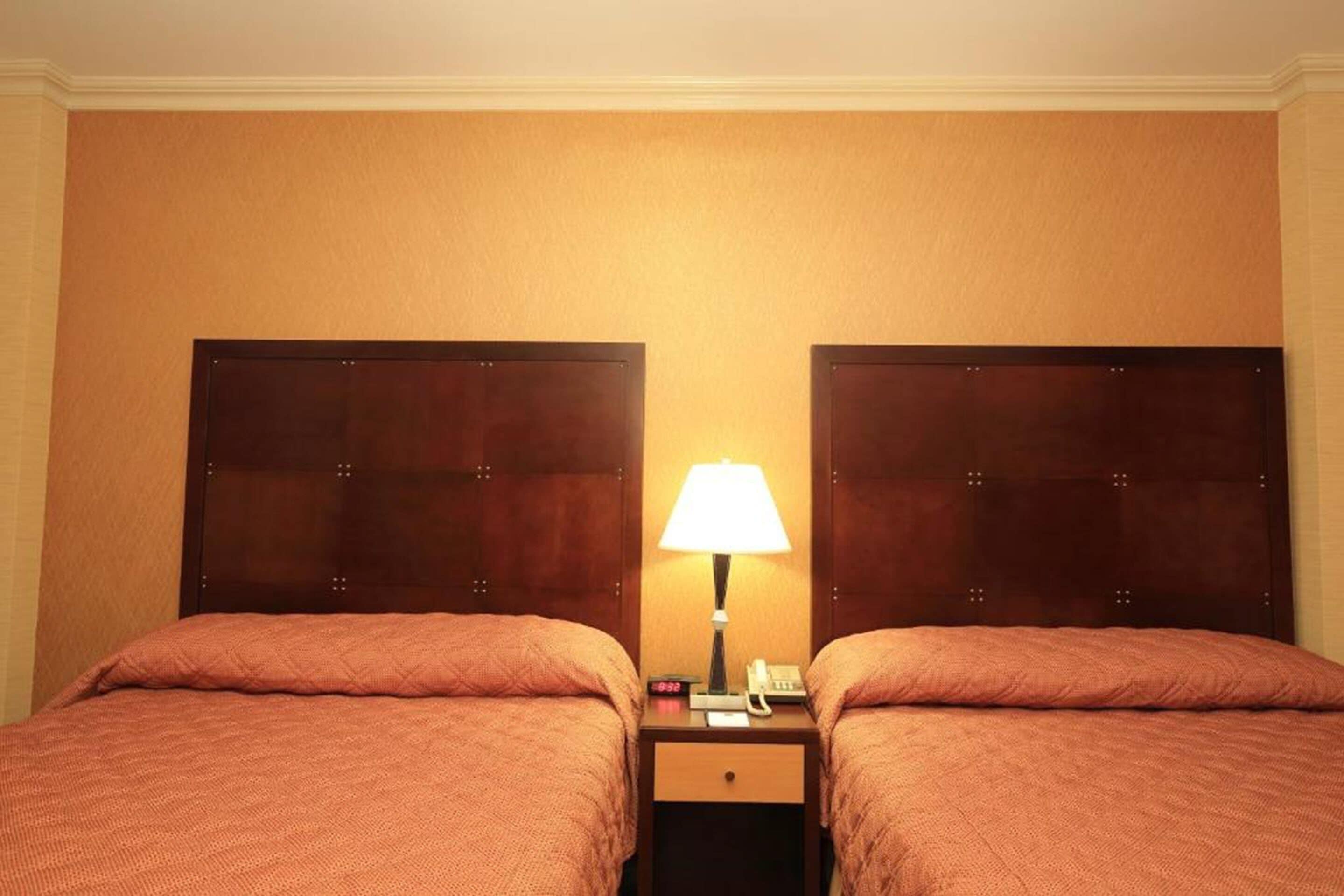 A hotel room with two beds, a nightstand with a lamp, and a small drawer.