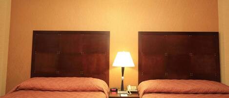 A hotel room with two beds, a nightstand with a lamp, and a small drawer.