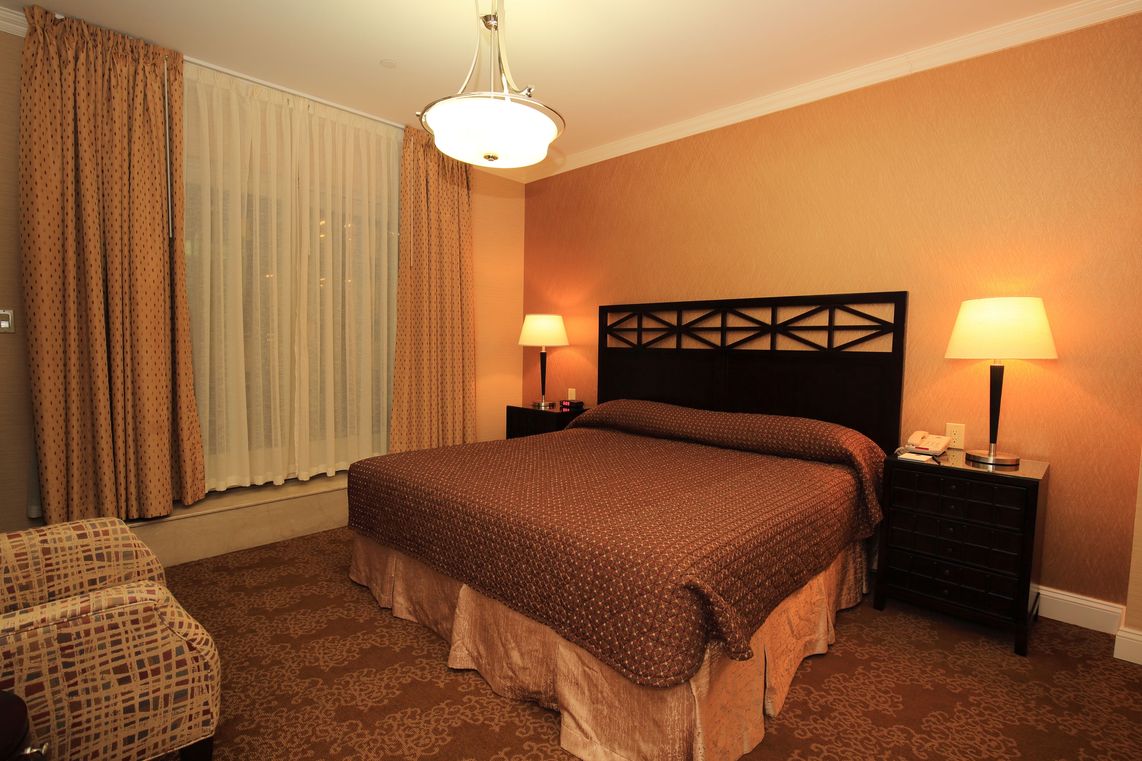 A hotel room with a large bed, two bedside tables with lamps, a chair, and a window with curtains.