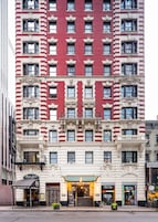 Um edifício de vários andares com fachada vermelha e branca, apresentando uma entrada no nível da rua com a placa 'Pasta Lovers' e 'Bombay Toast'.