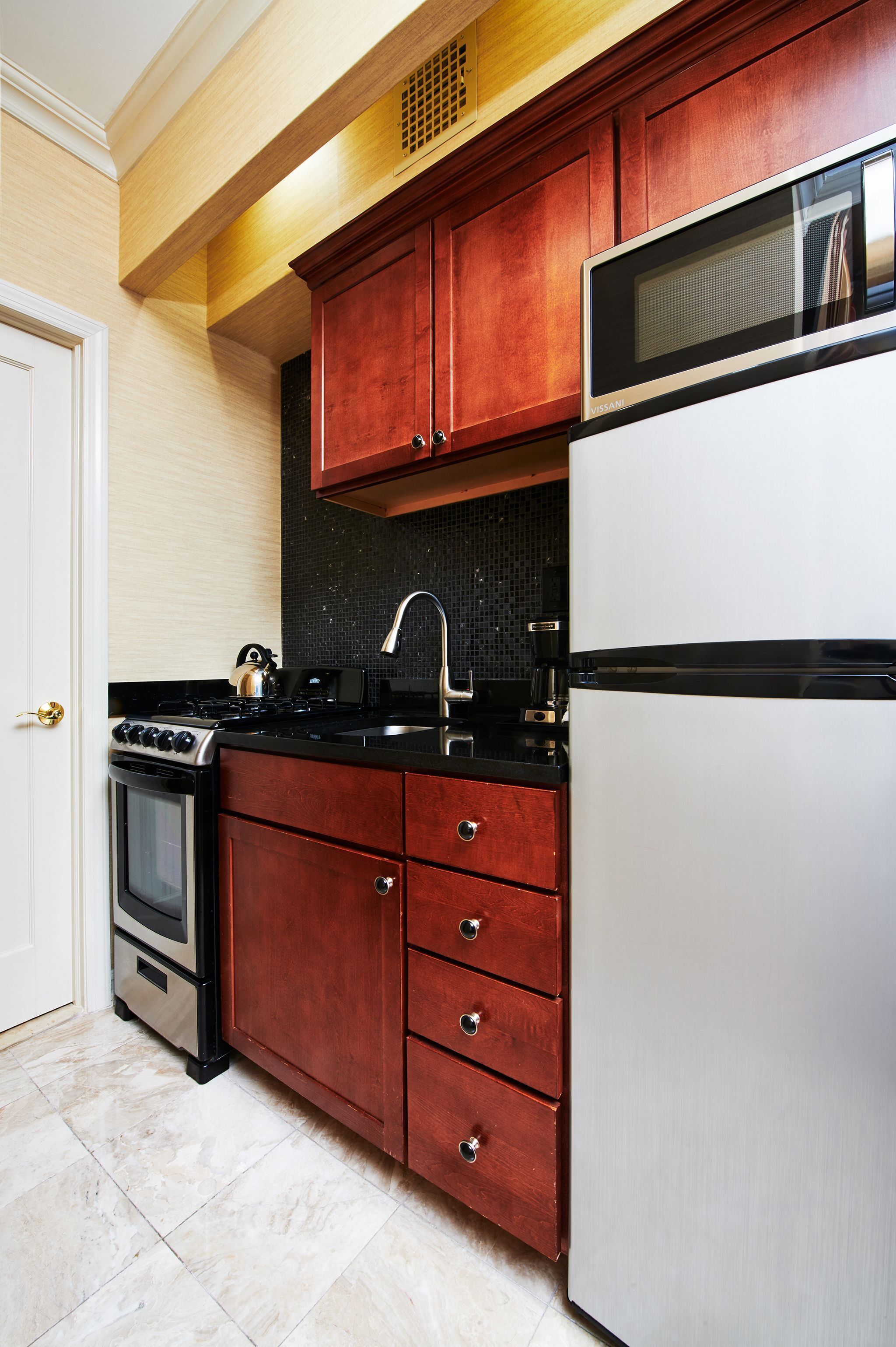A kitchen with wooden cabinets, a stainless steel refrigerator, a stove, and a microwave.