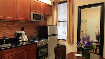 Una cocina compacta con armarios de madera, un microondas, una estufa y un refrigerador. Hay una mesa de comedor con una silla y un jarrón de flores.
