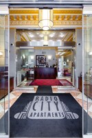 Um saguão de hotel com balcão de recepção, tapete vermelho e uma placa com a inscrição 'Radio City Apartments'.