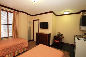 Quarto de hotel com duas camas, televisão, penteadeira, escrivaninha e cozinha compacta.