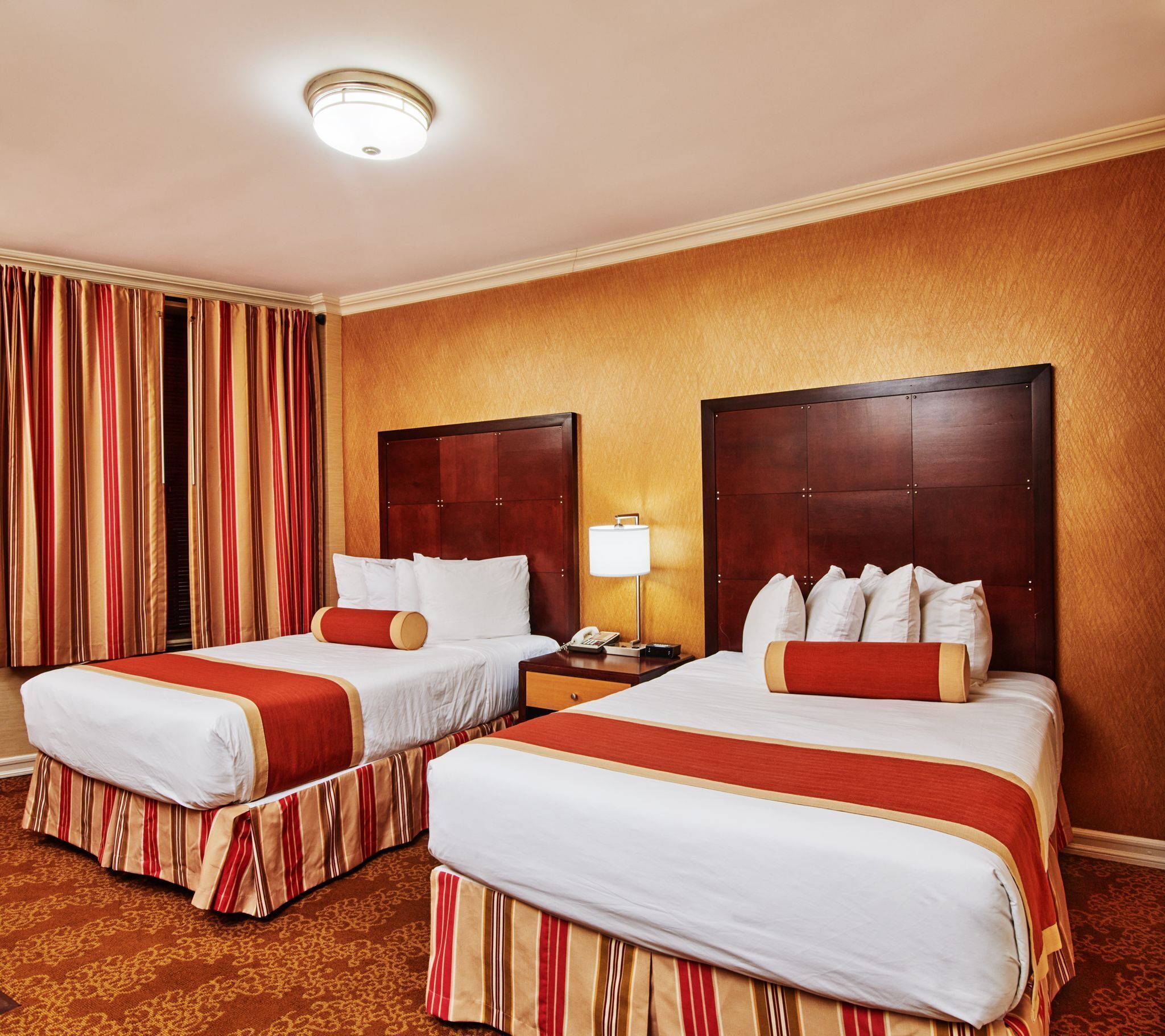A hotel room with two beds, a nightstand, a lamp, and a window with curtains.