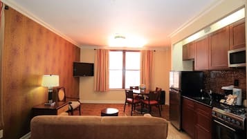 Ett kompakt bostadsutrymme med en soffa, ett matbord, stolar, en TV och ett köksområde med spishäll, mikrovågsugn och kylskåp.