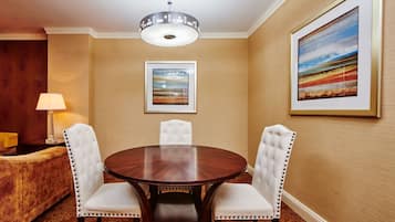 A dining area with a round table, four upholstered chairs, a chandelier, and two framed artworks on the walls.