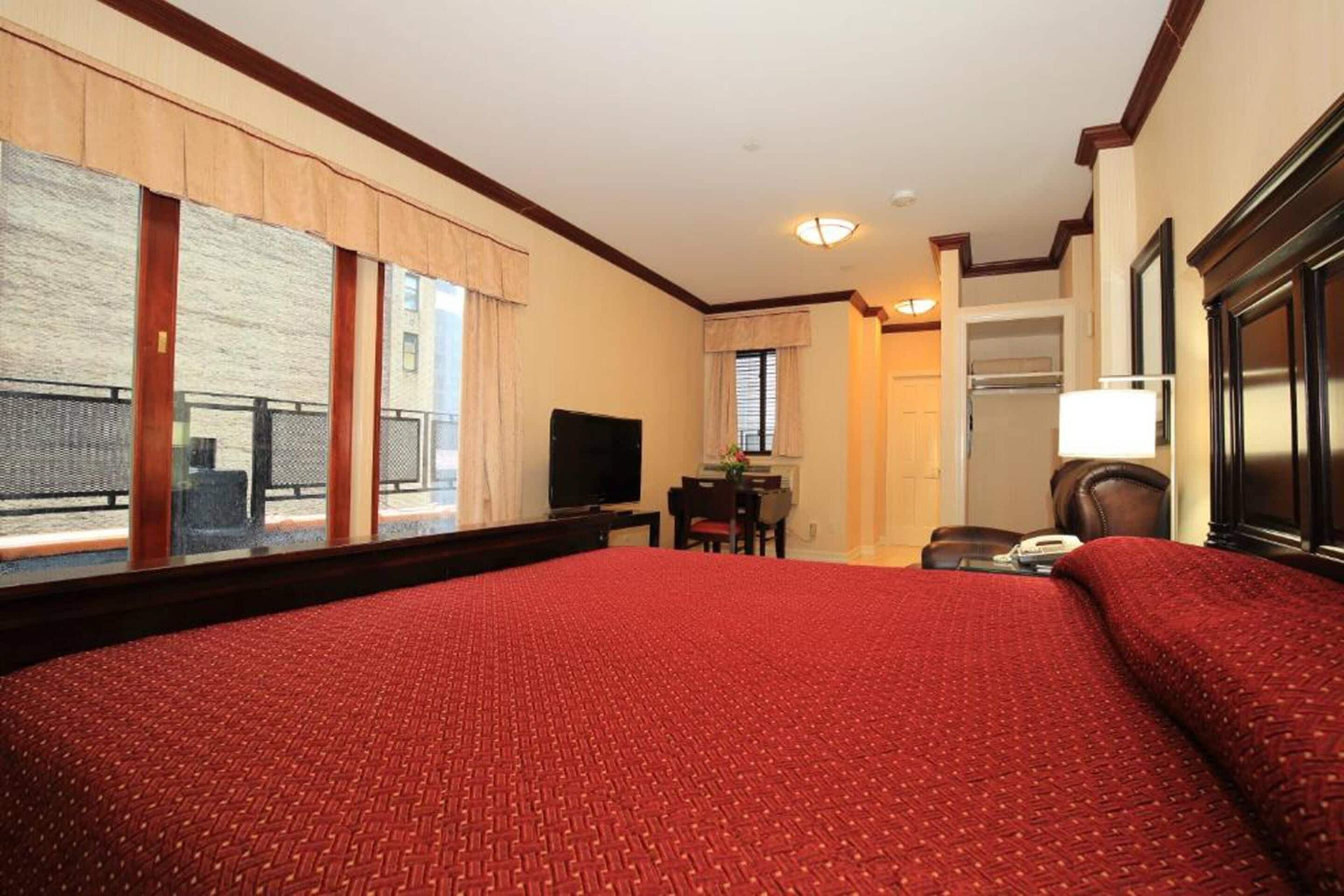 A hotel room with a large bed, a desk with a chair, a television, and a view of the outside balcony.