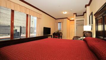 A hotel room with a large bed, a desk with a chair, a television, and a view of the outside balcony.