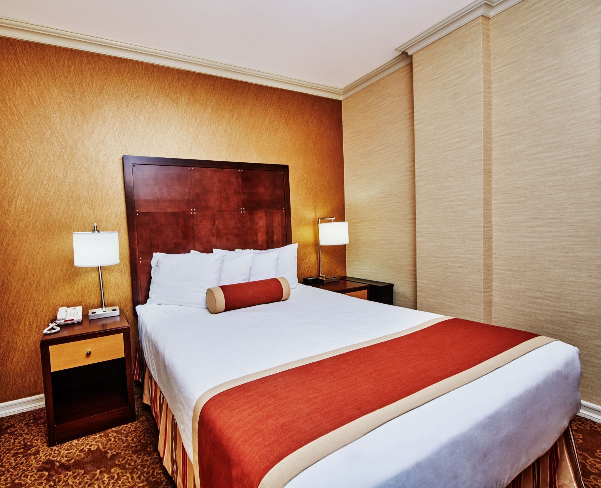 Una camera d'albergo con un letto grande, due comodini e un telefono fissato alla parete.