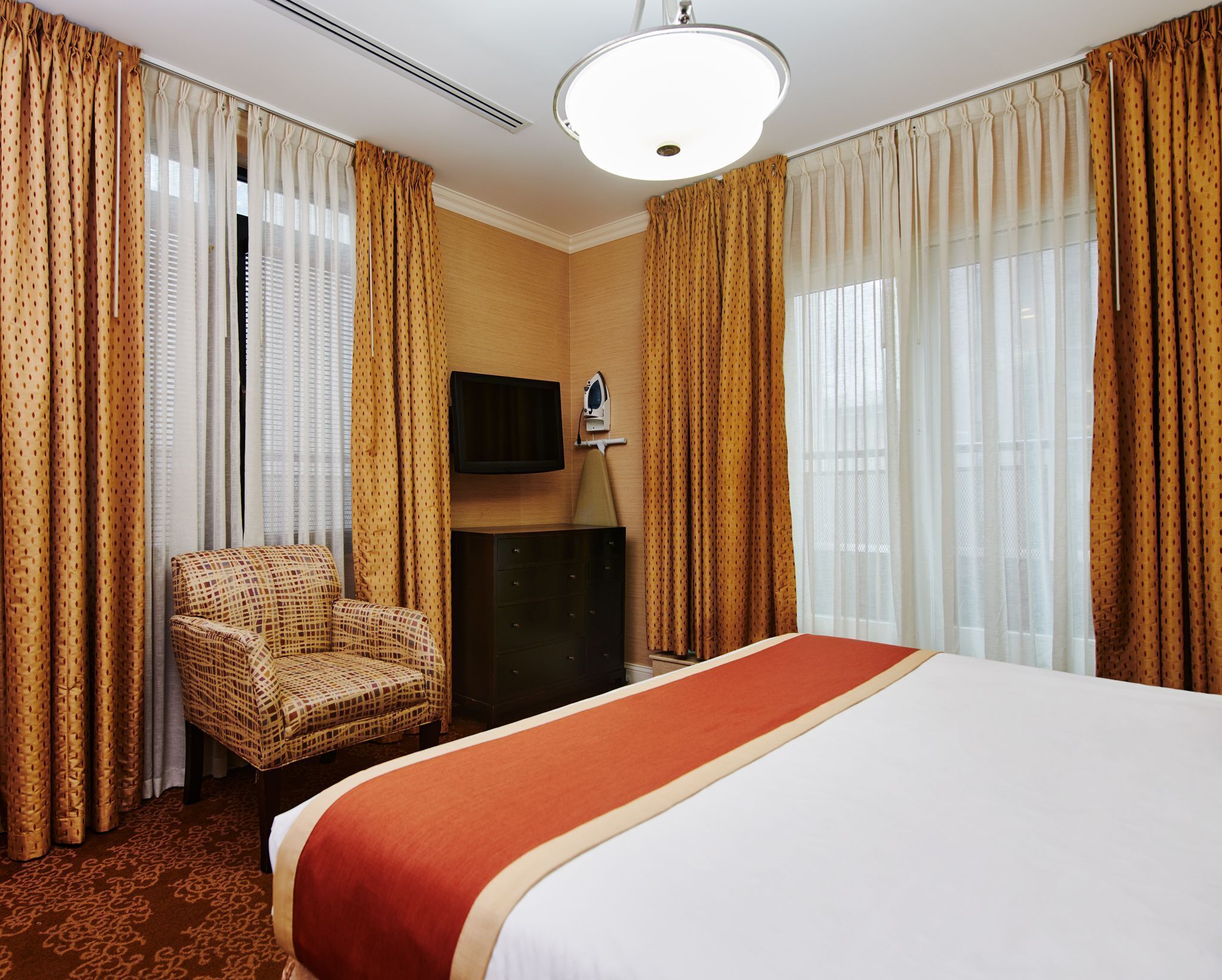 Ein Hotelzimmer mit einem großen Bett, einem Sessel, einem Flachbildfernseher und einem Schminktisch.
