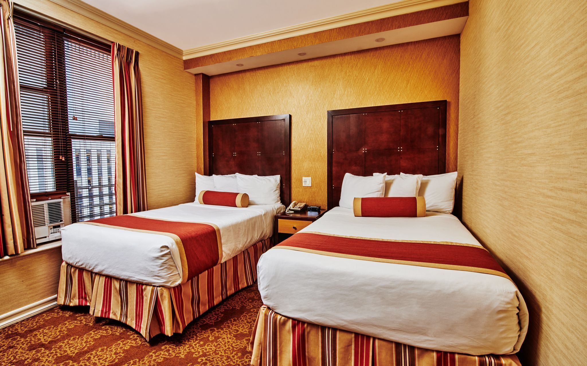 A hotel room with two beds, a wooden headboard, a telephone, and a window with blinds.
