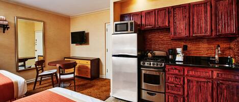 Une chambre d’hôtel compacte comprenant un coin cuisine, un espace repas avec une table et des chaises, et un lit avec une literie à rayures.