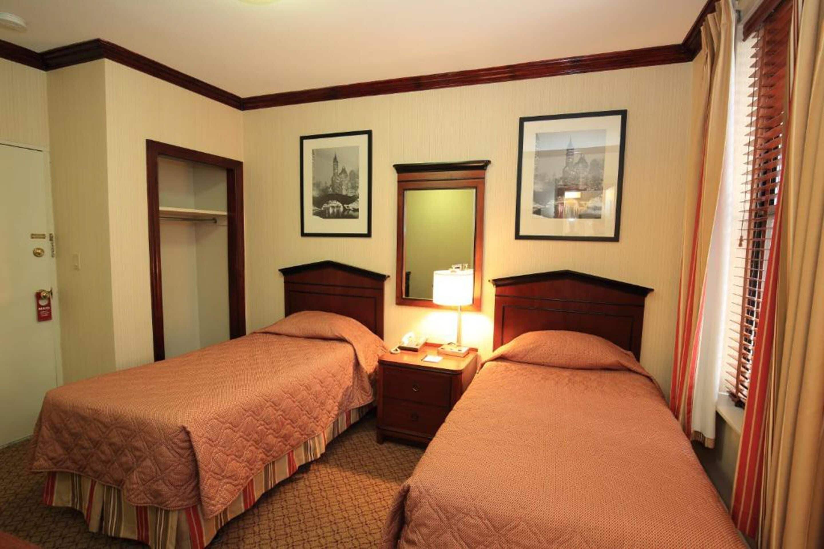 A hotel room with two beds, a nightstand, a mirror, and framed pictures on the wall.