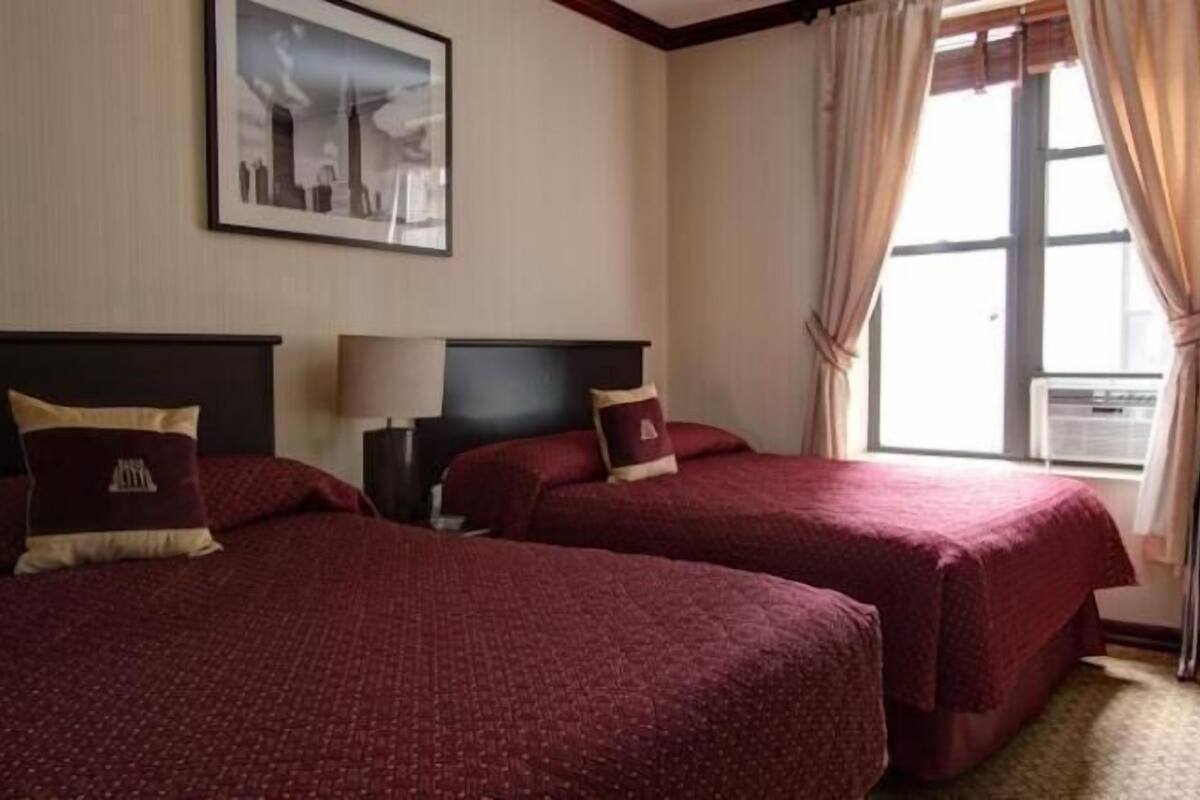 A hotel room with two beds, a window with curtains, a wall-mounted picture, and a radiator.