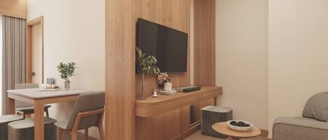 A modern living room with a wooden accent wall, a flat-screen TV mounted above a wooden console, a dining area with a table and chairs, and a round coffee table with a bowl of pinecones.