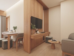 A modern living room with a wooden accent wall, a flat-screen TV mounted above a wooden console, a dining area with a table and chairs, and a round coffee table with a bowl of pinecones. - Victoria Nimman Hotel (Chiang Mai)