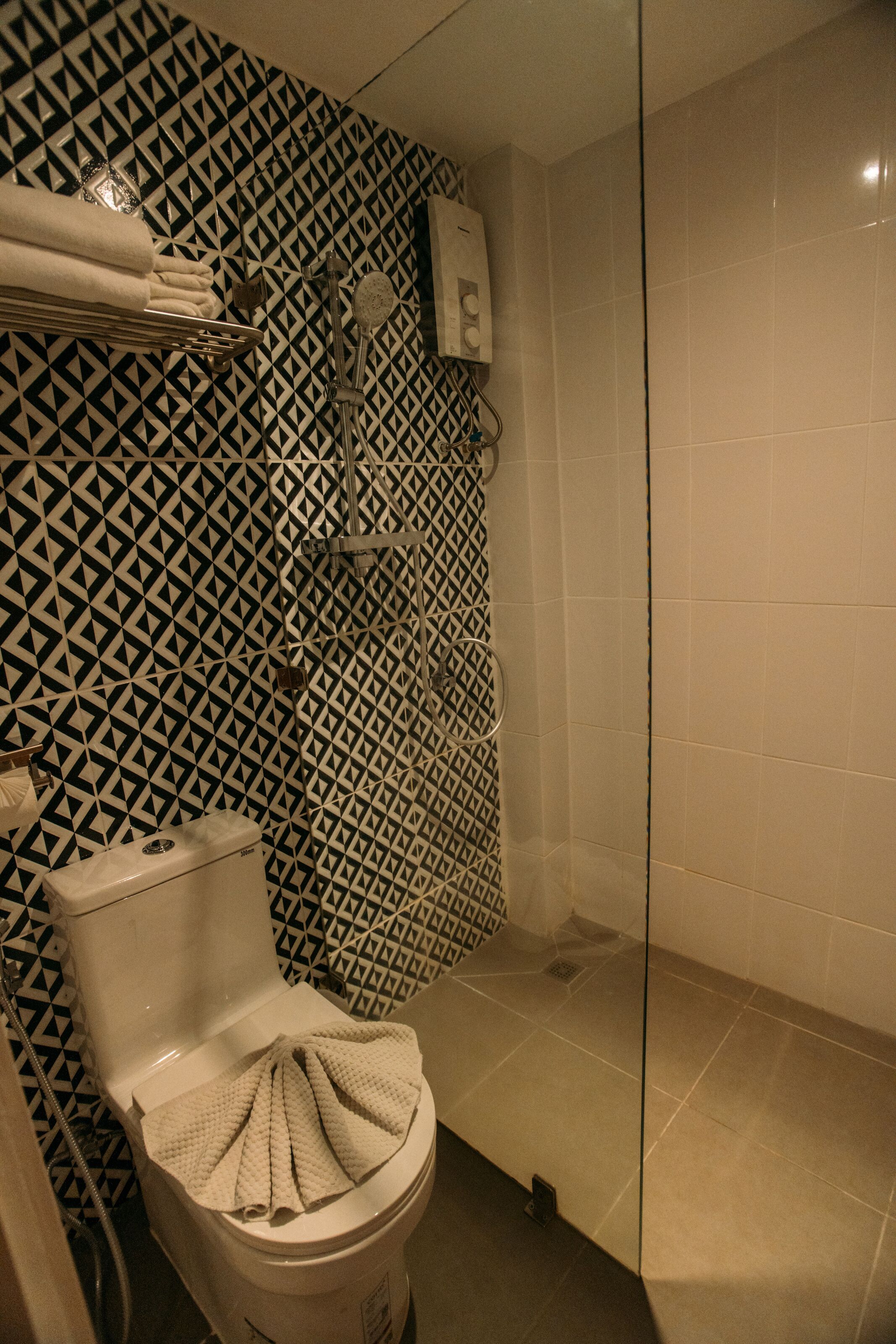 A bathroom with a patterned wall, a toilet, a shower, and a glass partition.