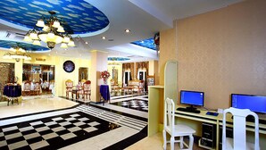 A hotel lobby with a checkered floor, a chandelier, and a desk with two monitors.
