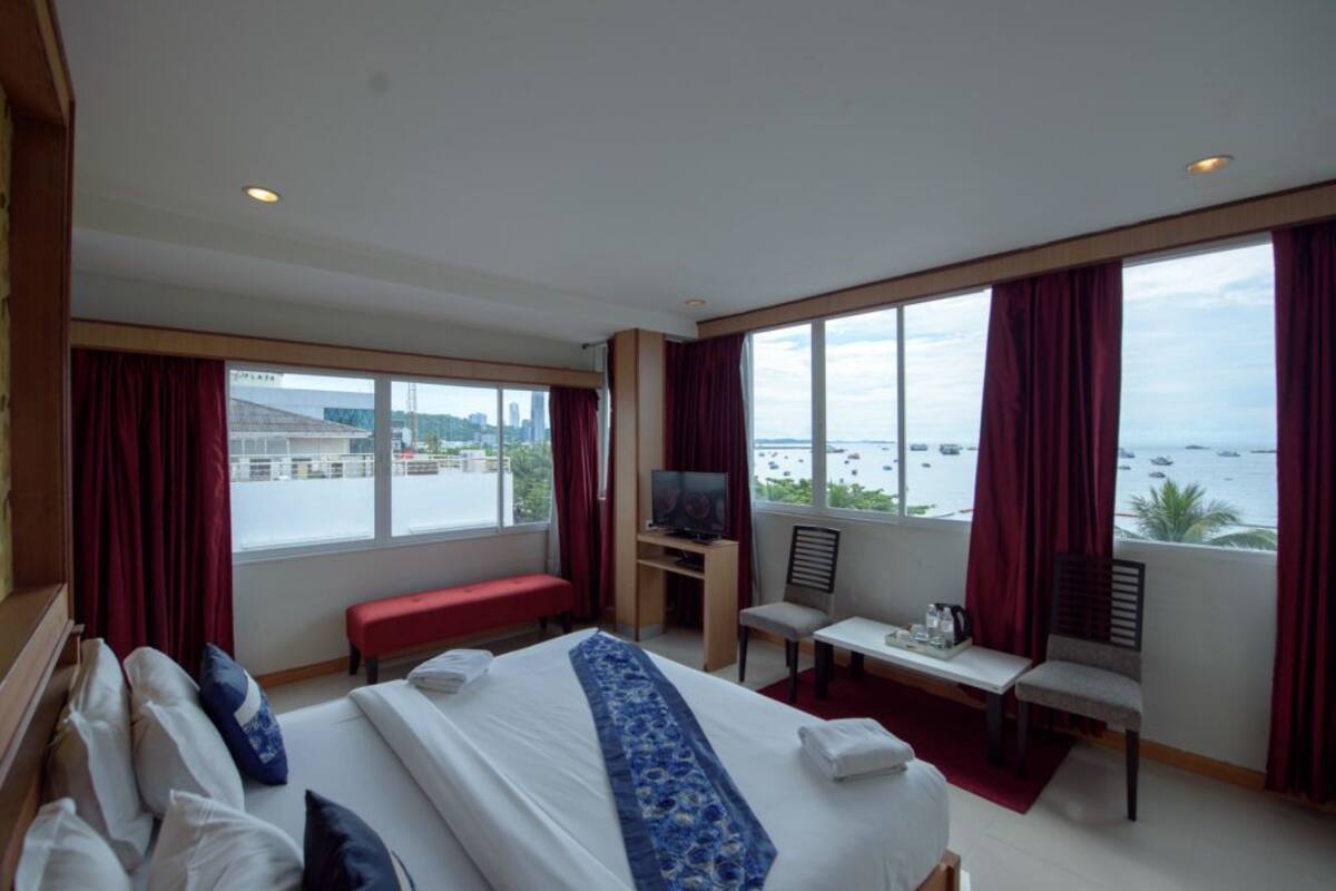 Ein Hotelzimmer mit einem großen Bett, einem Schreibtisch, einem Sessel, einem Fernseher und Meerblick.