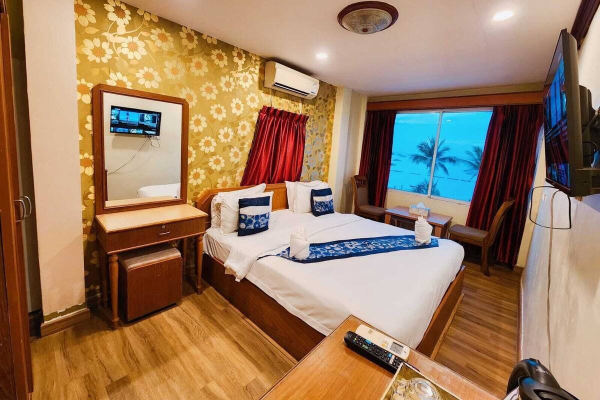 Ein Hotelzimmer mit Bett, Schreibtisch, Fernseher und Fenster mit Blick auf Palmen.