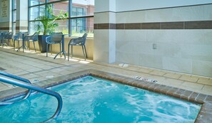 Una piscina con borde de azulejos, rodeada de sillones de descanso y una planta en maceta.