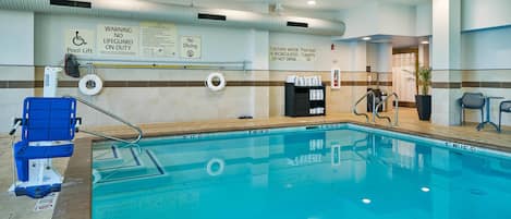 Una piscina interior con elevador para discapacitados, señal de prohibido bucear y advertencia sobre recirculación de agua.