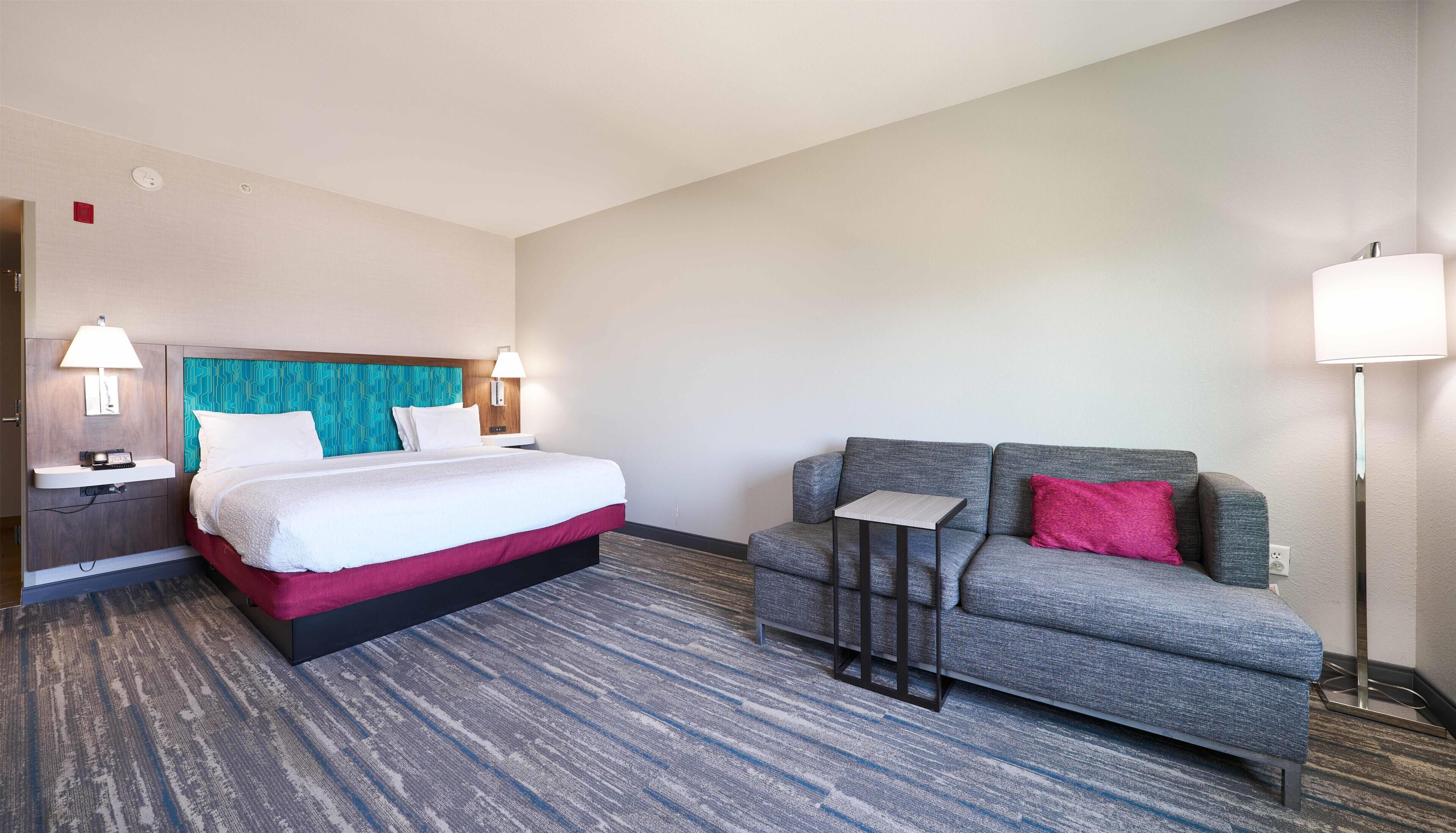 A hotel room with a bed, a sofa, a nightstand, and a lamp.