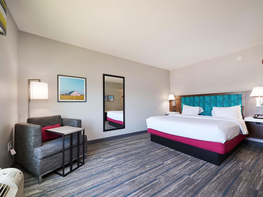 A hotel room with a bed, a chair, a desk, a mirror, and a picture on the wall.