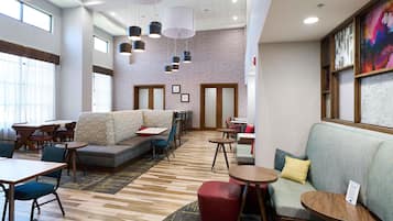 Un hall d’hôtel moderne, doté d’un espace salon, de tables et d’un tapis à motifs.