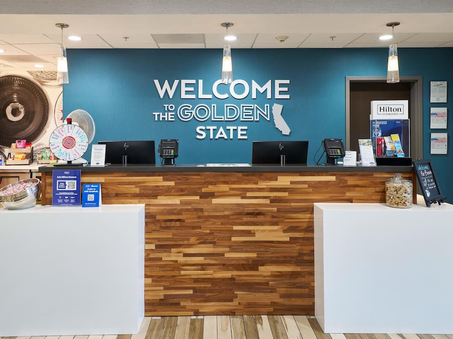 A reception desk with a 'Welcome to the Golden State' sign, a fan, and a 'Hilton Honors' sign.