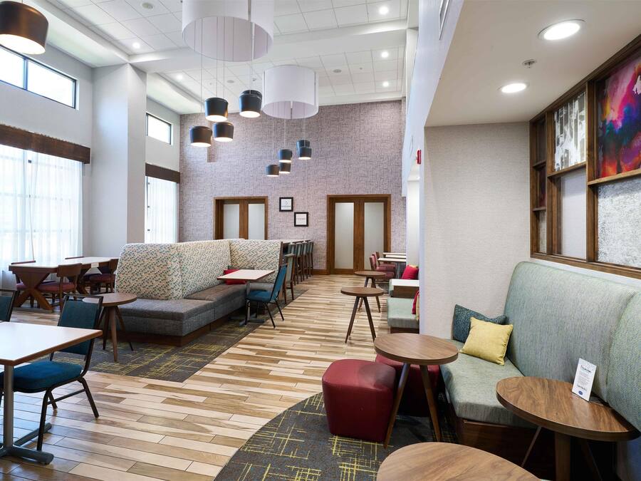 A modern hotel lobby with a seating area, tables, and a patterned carpet.