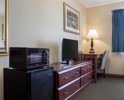 Habitación de hotel con microondas, televisor, escritorio con lámpara, silla y cómoda.