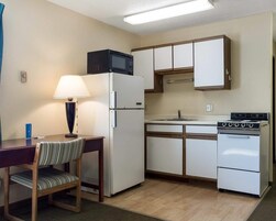 Una kitchenette compacta con refrigerador, microondas, estufa y un pequeño comedor con una silla y una mesa.