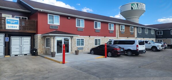 A hotel with a red exterior, a lobby entrance, and a parking area with several vehicles.