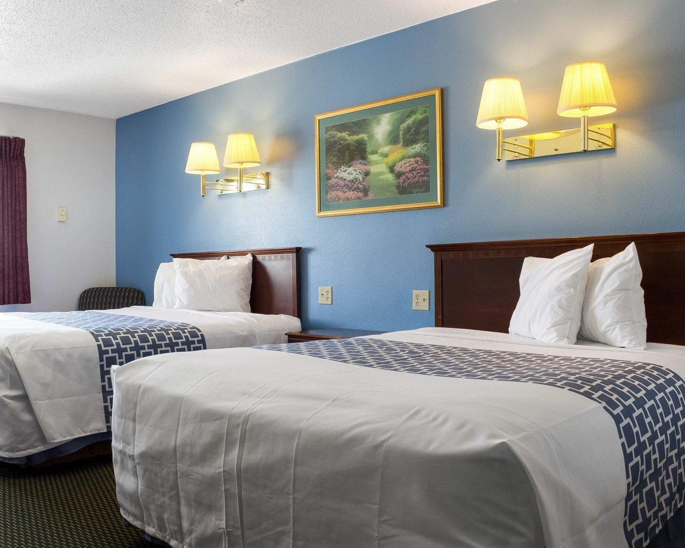 A hotel room with two beds, a painting on the wall, and wall-mounted lamps.
