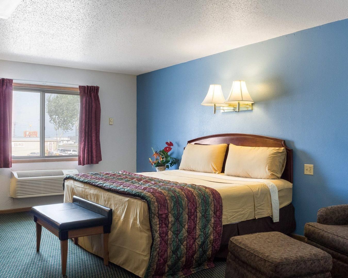 A hotel room with a bed, a chair, a desk, and a window with curtains.