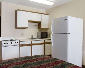 A compact kitchen with white cabinets, a microwave, a refrigerator, and a stove.