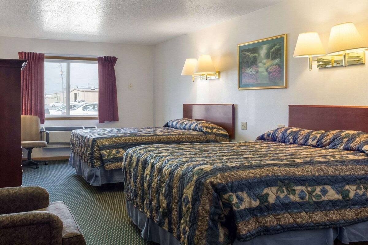 Ett hotellrum med två sängar, ett skrivbord, en stol och ett fönster med gardiner.