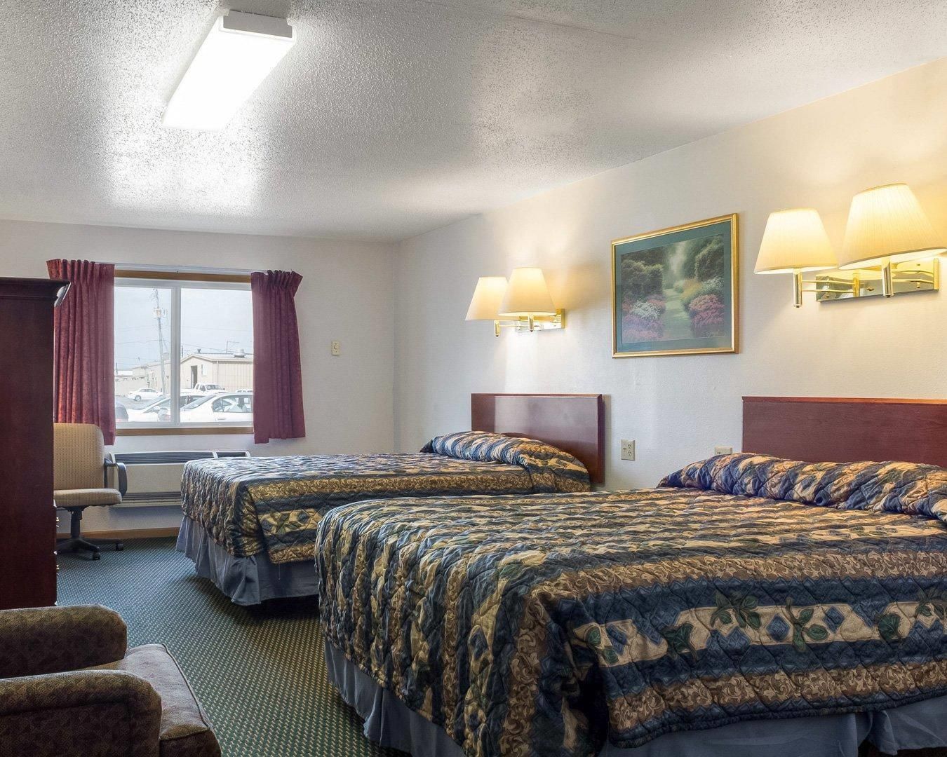 A hotel room with two beds, a desk, a chair, and a window with curtains.