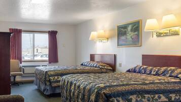 A hotel room with two beds, a desk, a chair, and a window with curtains.