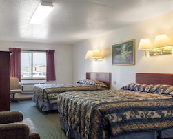 Una habitación de hotel con dos camas, un escritorio, una silla y un ventanal con cortinas.