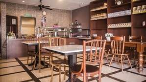 A restaurant with wooden chairs and tables, a kitchen area, and shelves with packaged goods. - AG Hotel Penang (George Town)