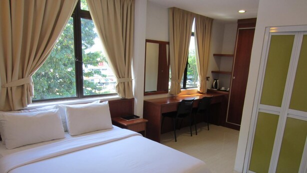 A hotel room with a bed, a desk, a chair, a mirror, and a view of the outside. - AG Hotel Penang (George Town)