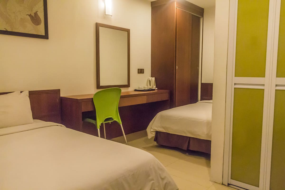 A hotel room with two beds, a desk, a chair, a mirror, and a wardrobe.