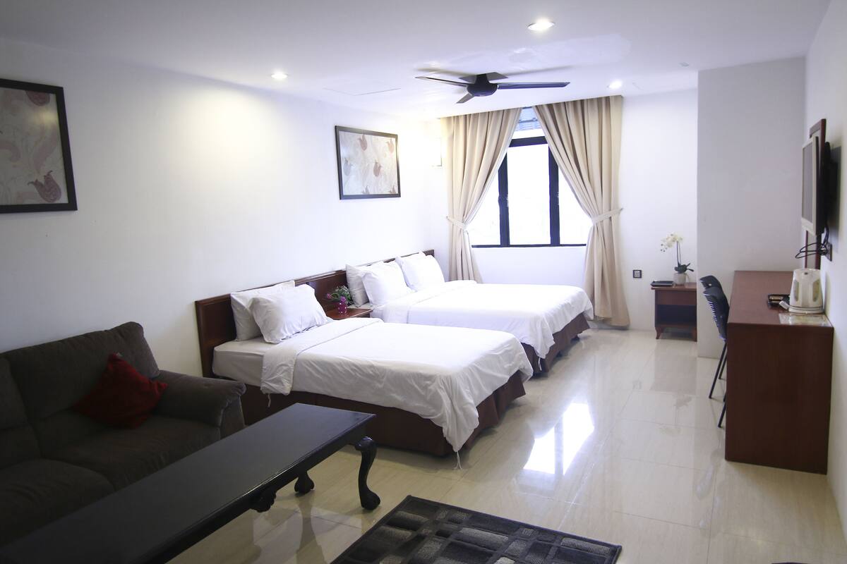 A hotel room with two beds, a desk, a TV, and a ceiling fan.