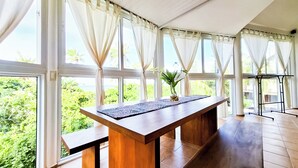 A spacious room with large windows, a wooden table, and a potted plant.